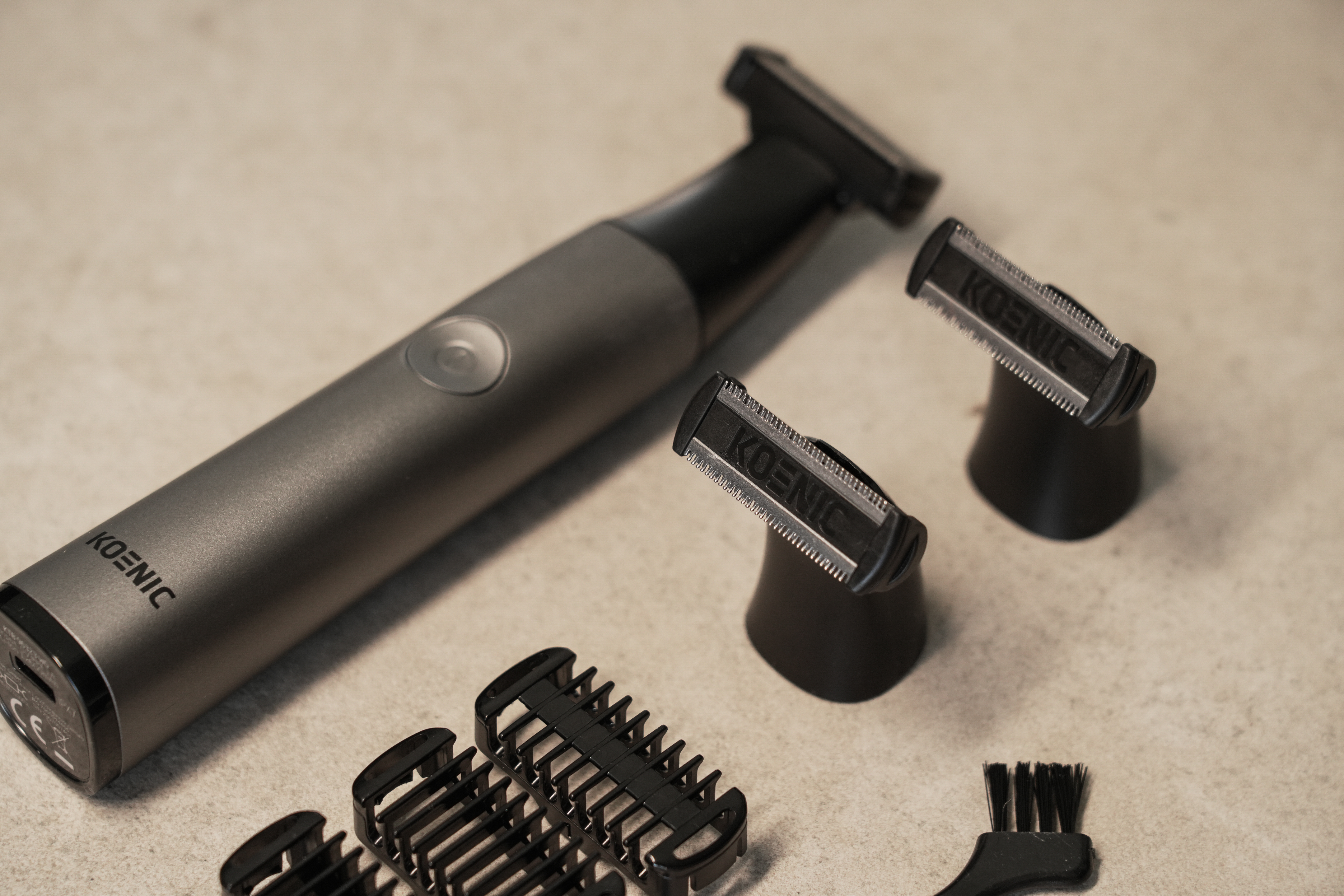 Szary trymer z nasadkami i szczoteczką na jasnym podłożu.