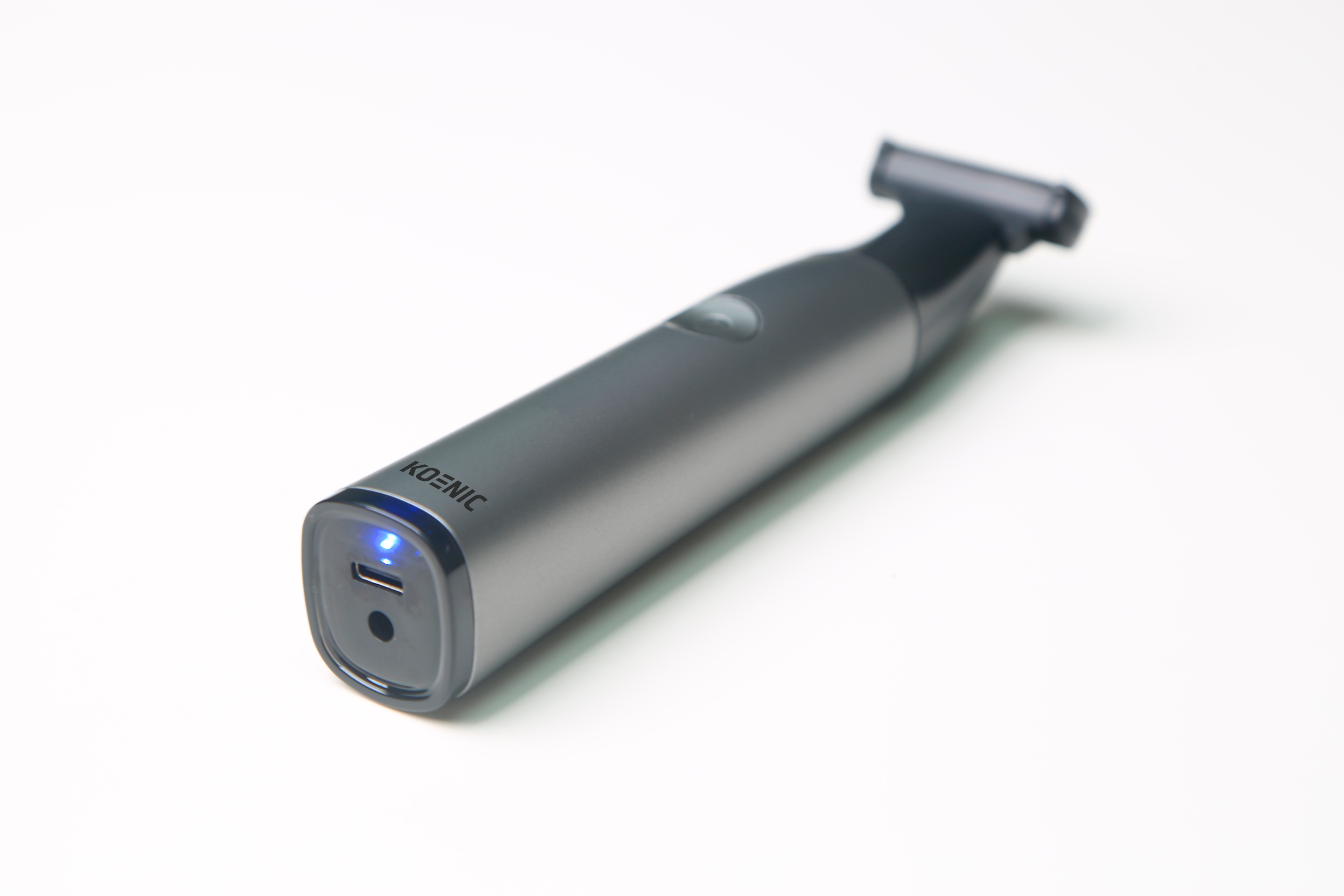 Szary trymer z niebieskim światłem na porcie ładowania USB, na białym tle.