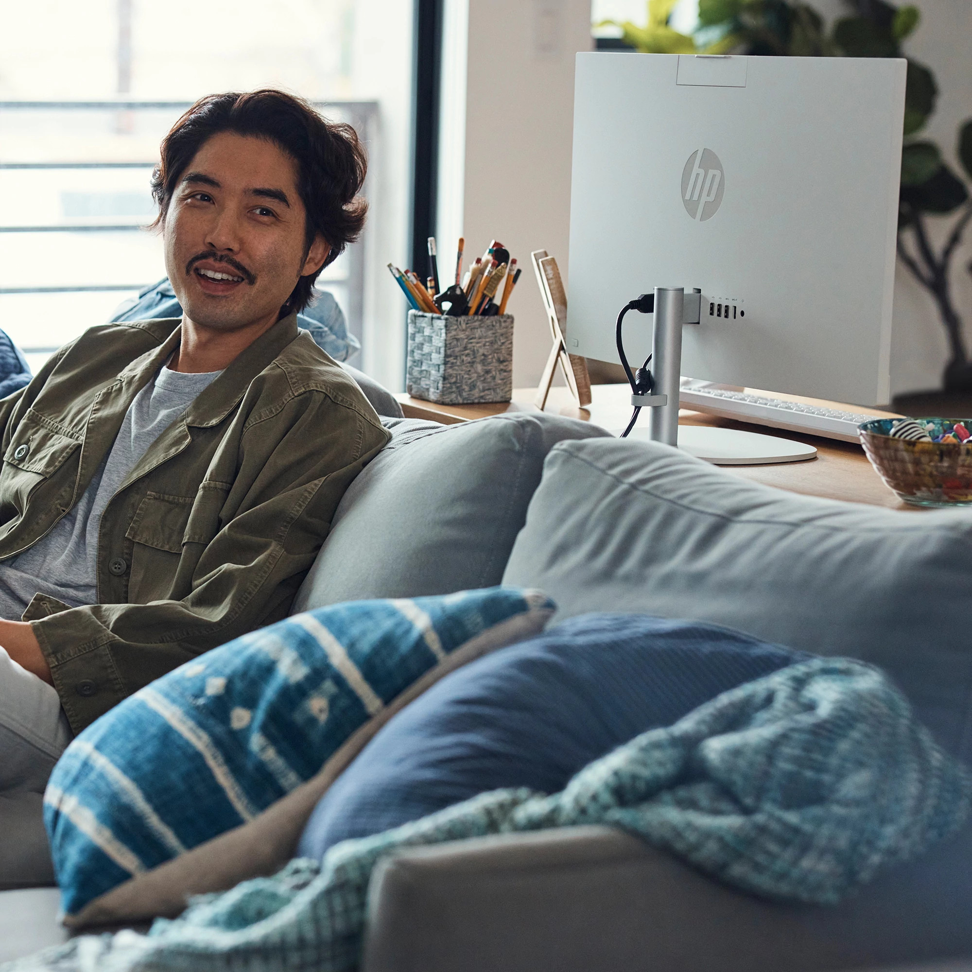 Mężczyzna z wąsami siedzi na kanapie przed komputerem.