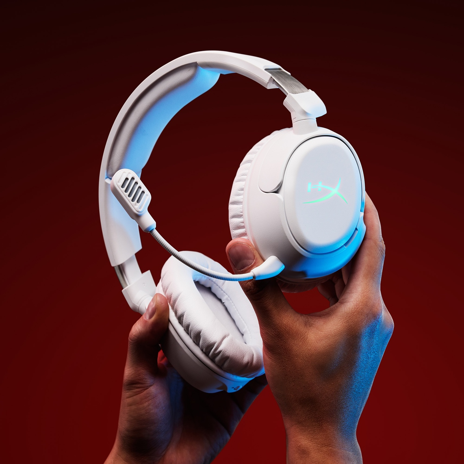Casque blanc avec micro tenu par des mains sur fond rouge.