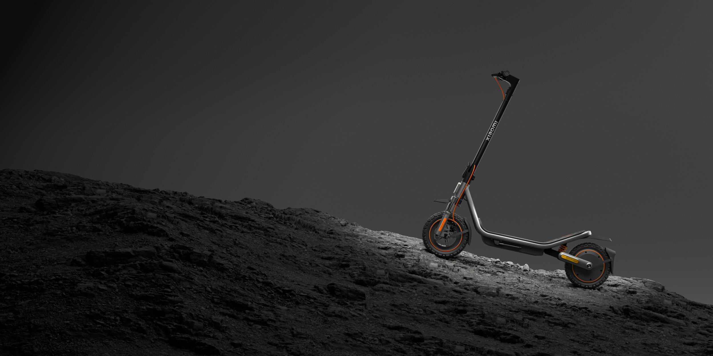Ein grauer Xiaomi E-Scooter mit orangefarbenen Akzenten steht auf felsigem Gelände.