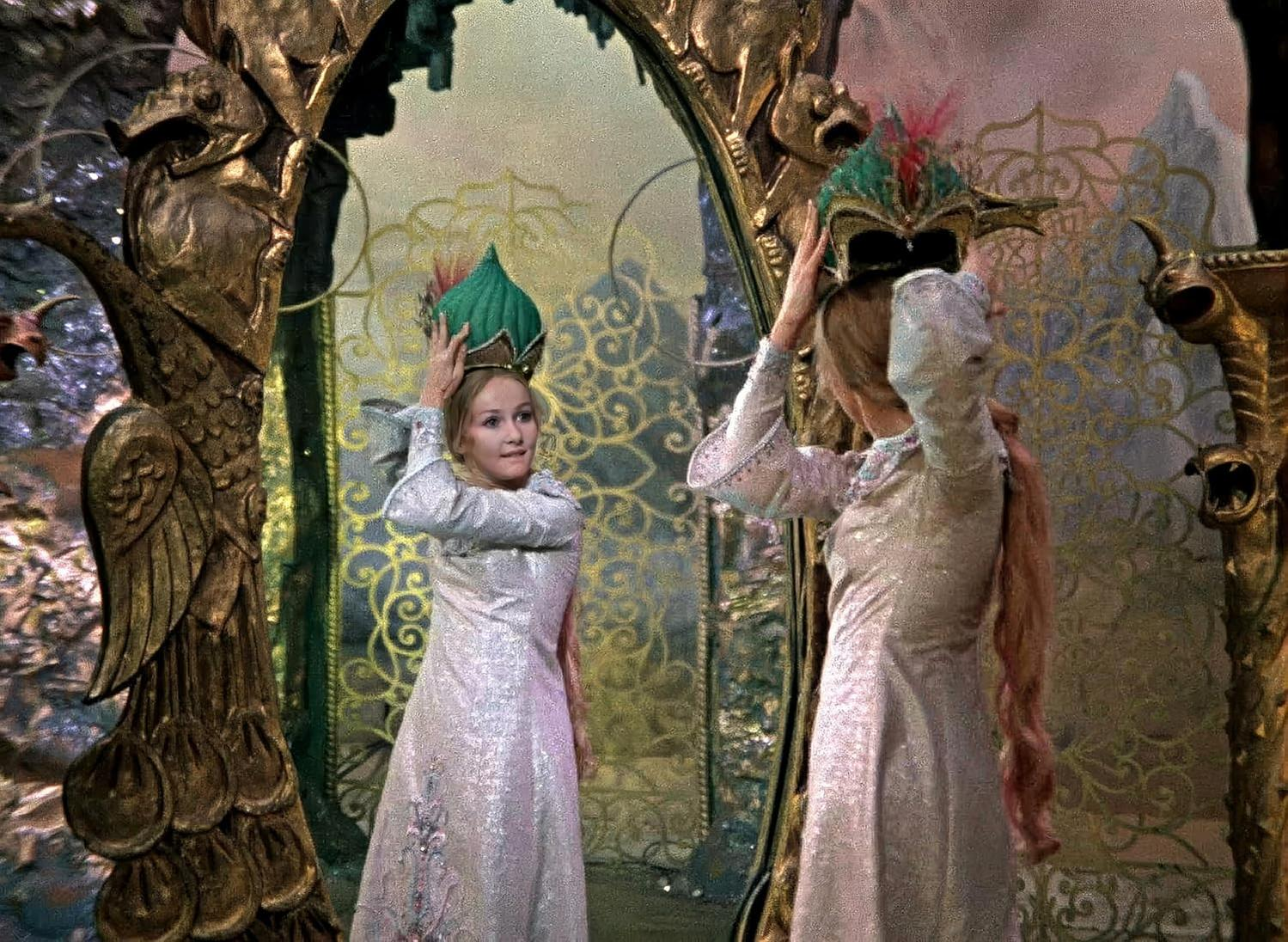 Zwei Frauen in glitzernden Kleidern und Hüten vor einem goldenen Tor.