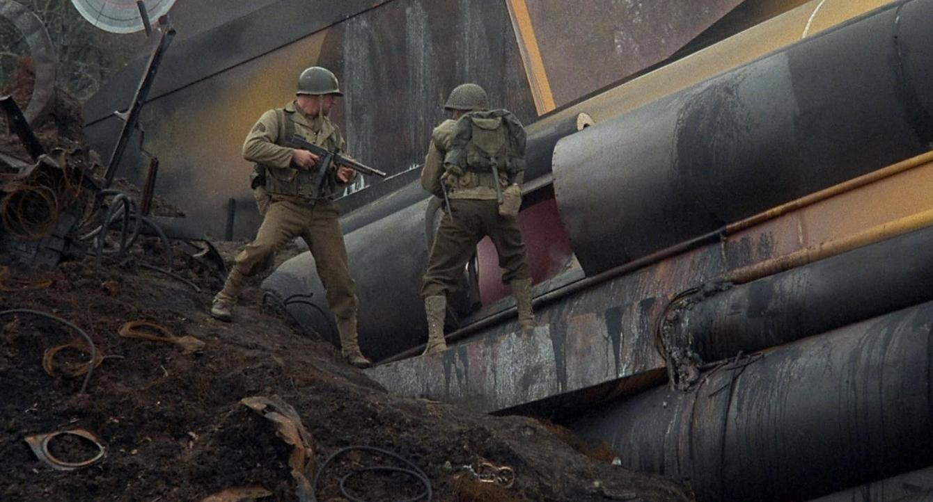 Zwei Soldaten in Uniformen stehen auf einem Haufen Schutt neben großen schwarzen Rohren.