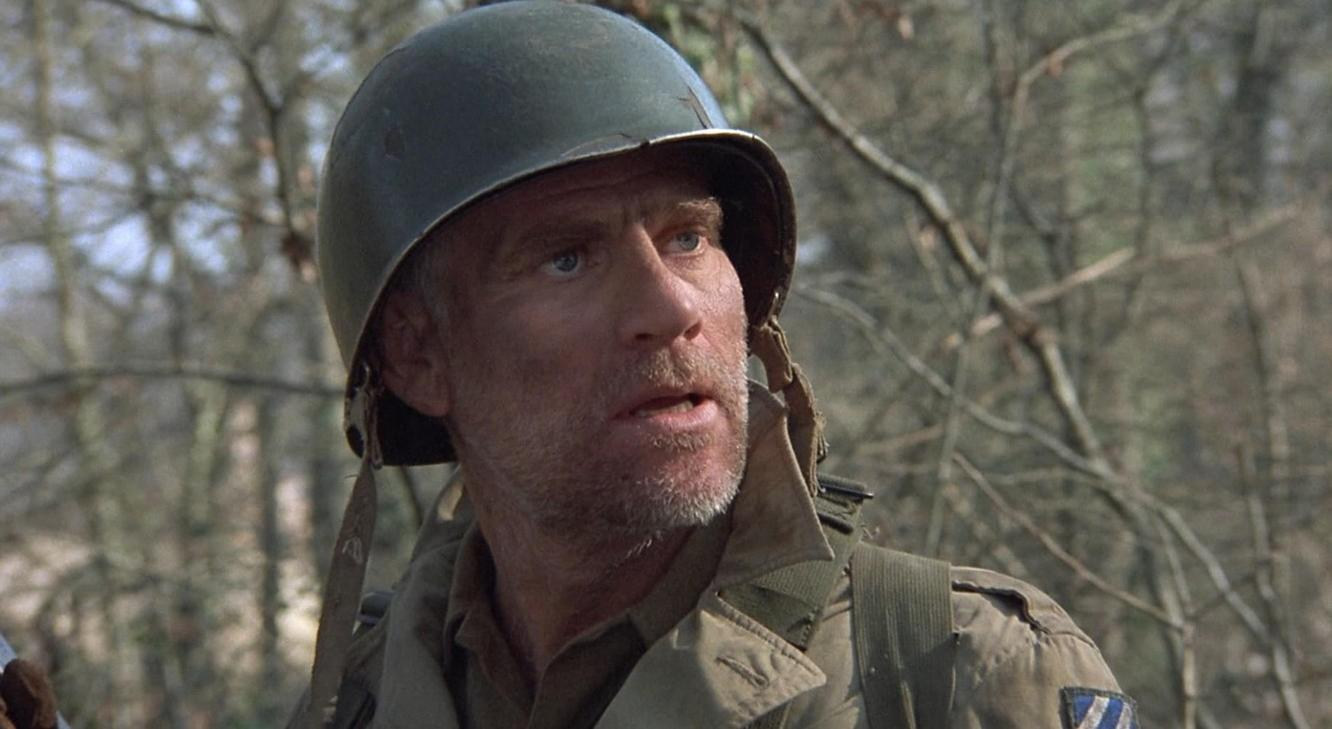 Ein Mann in Militäruniform mit Helm blickt nach rechts. Bäume im Hintergrund.