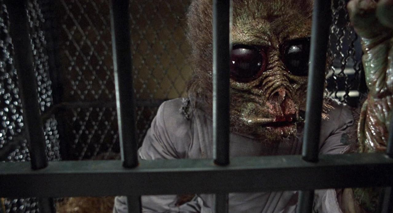 Ein gruseliges Wesen mit großen Augen sitzt hinter Gittern in einem Käfig.