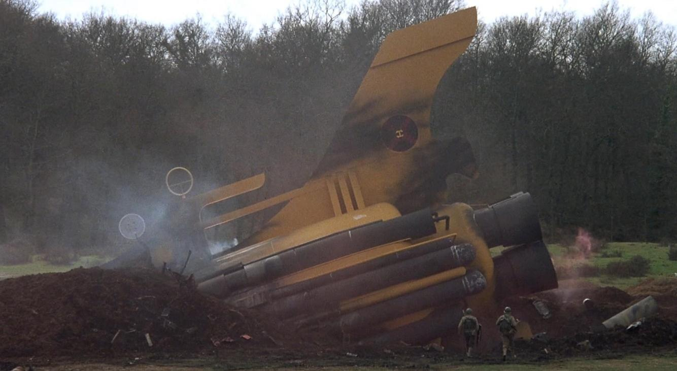 Gelbes abgestürztes Flugzeug mit Soldaten im Vordergrund, Rauch steigt auf.