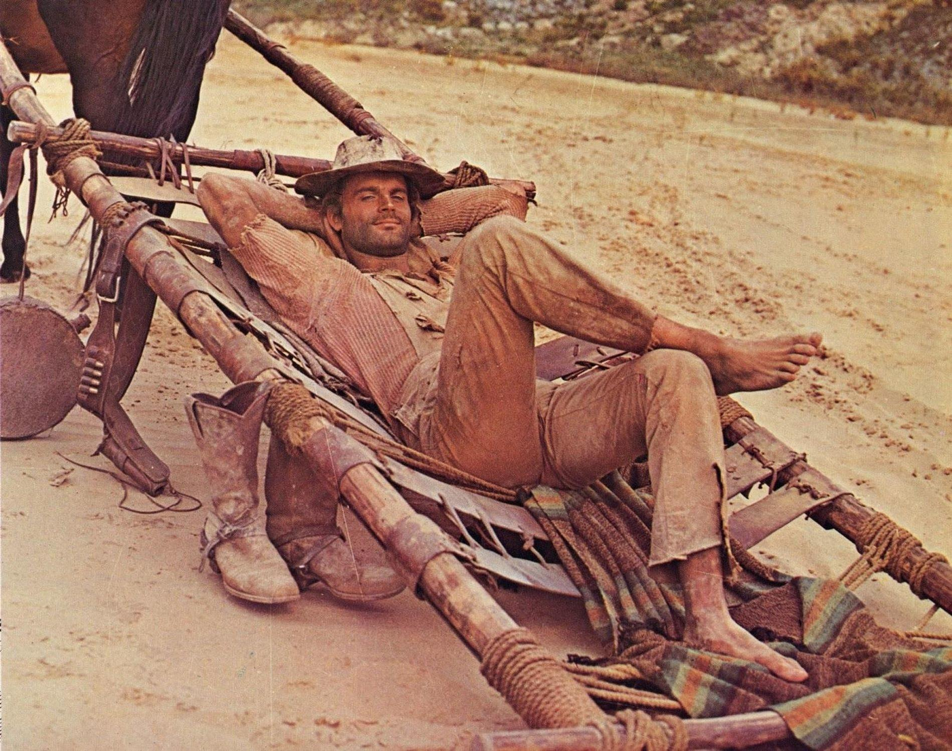Ein Mann in Cowboykleidung liegt in einer Hängematte neben einem Pferd.