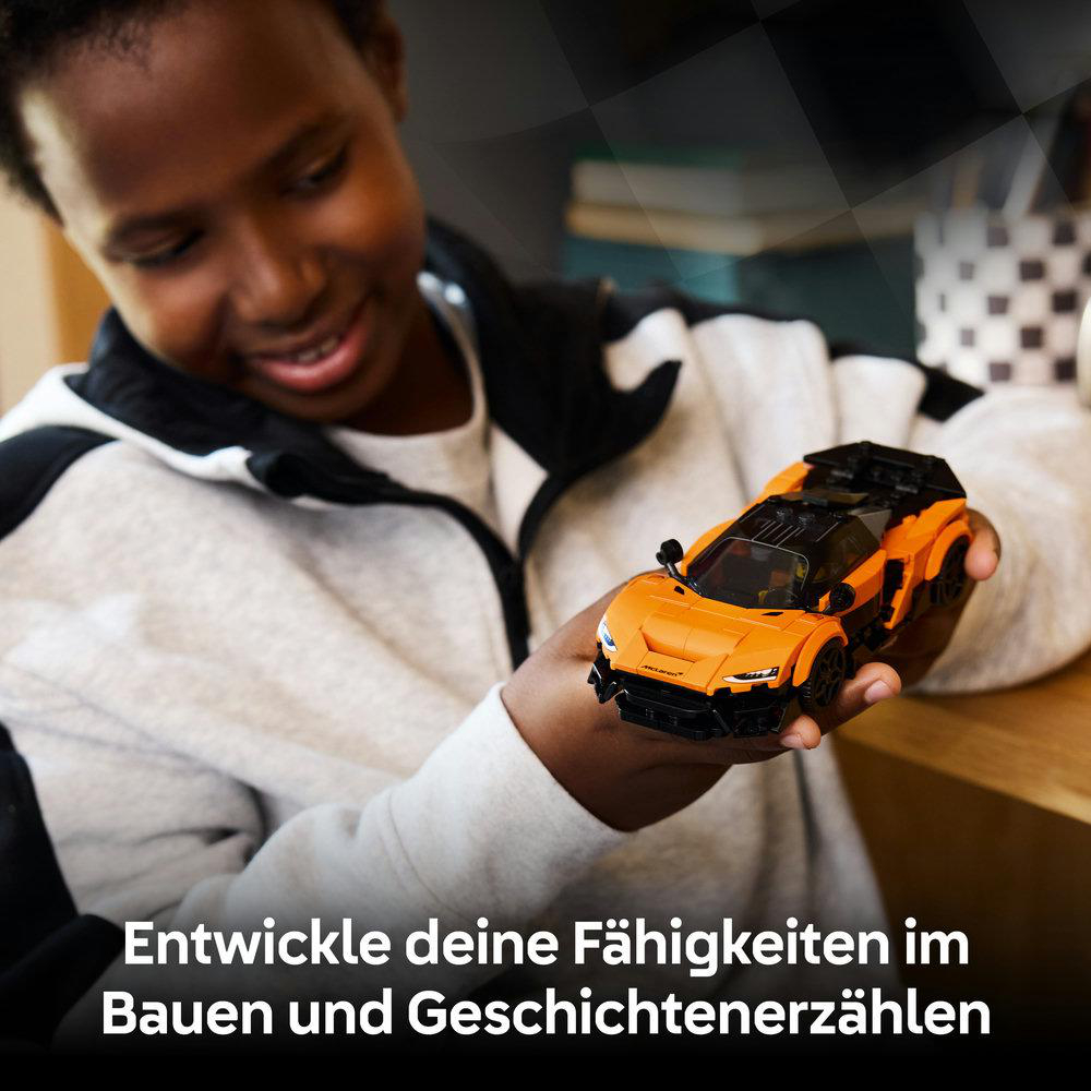 Junge hält orangefarbenes Spielzeugauto in der Hand, fokussiert auf das Bauen und Erzählen von Geschichten.