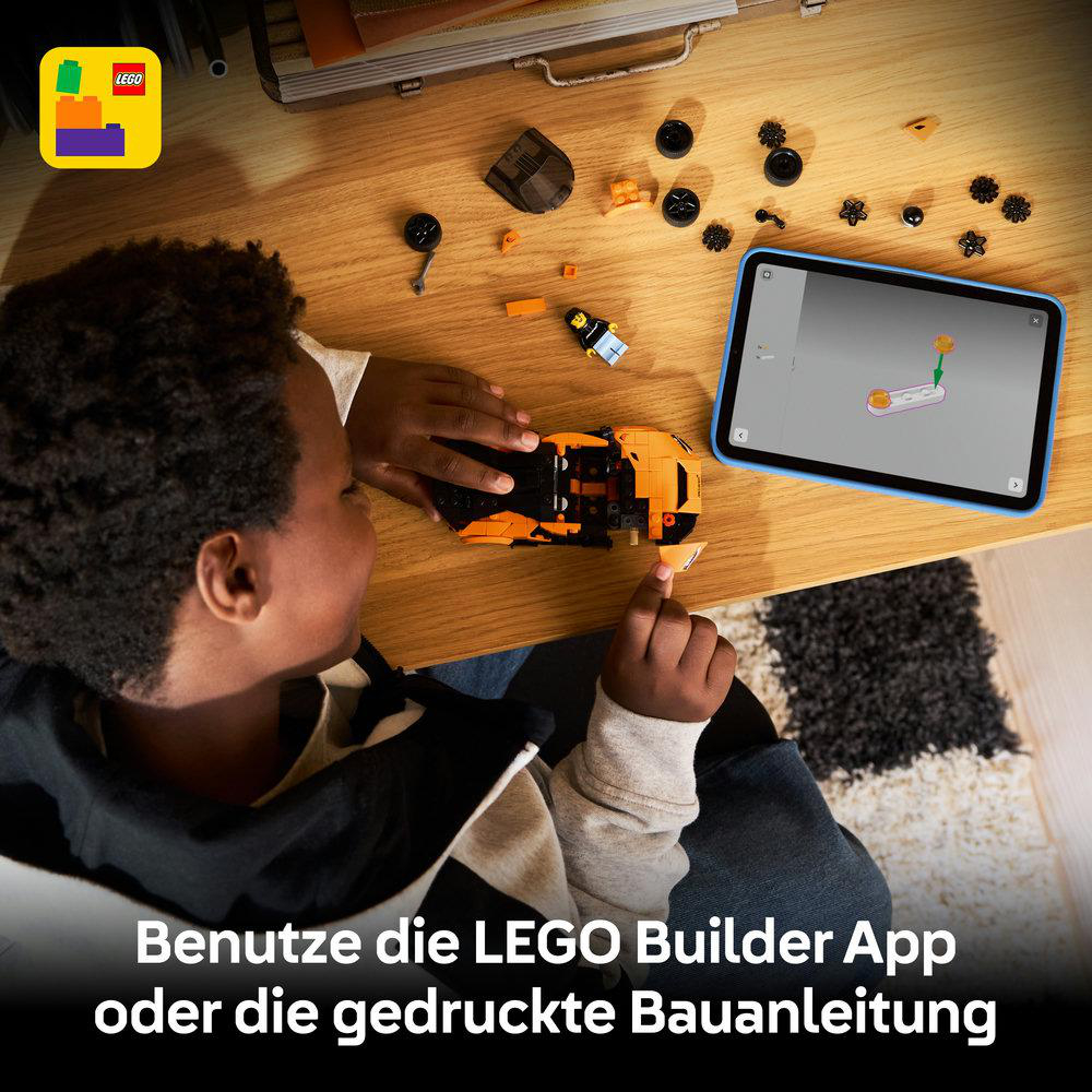 Kind baut orange LEGO-Auto neben Tablet mit Bauanleitung auf Holztisch.