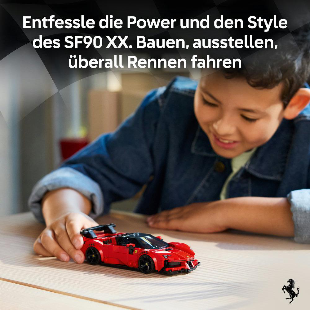 Ein Junge spielt mit einem roten Lego-Ferrari-Spielzeugauto auf einem Holztisch.