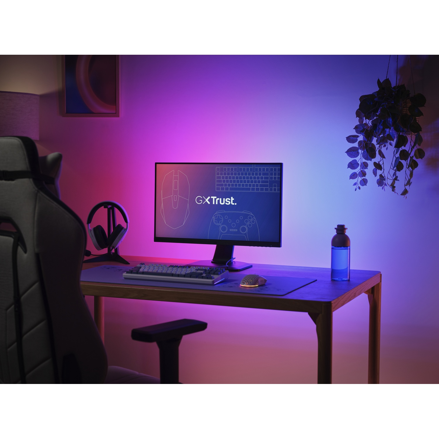 A desk with a gaming setup, illuminated by purple and pink light.