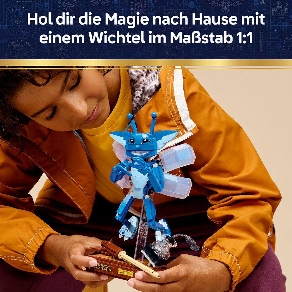 Ein Kind hält eine blaue Wichtelfigur aus LEGO mit Flügeln und einer Basis.