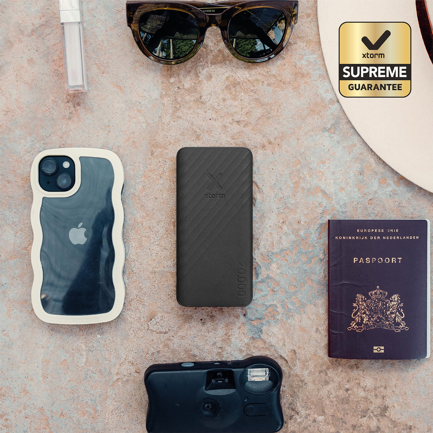 A black power bank, phone, sunglasses, passport, camera, and lipstick lie on a stone surface.