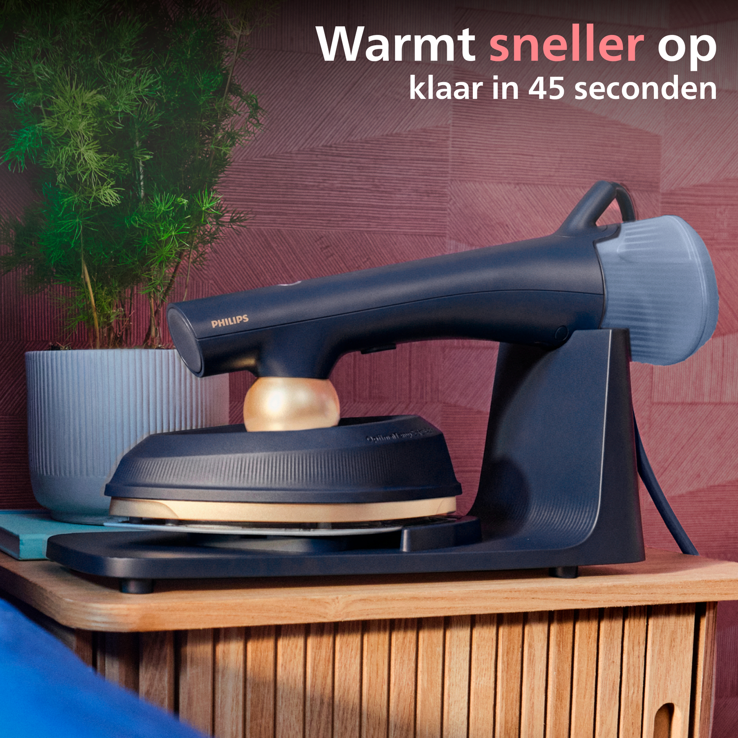 A dark blue garment steamer rests on a wooden cabinet next to a potted plant.