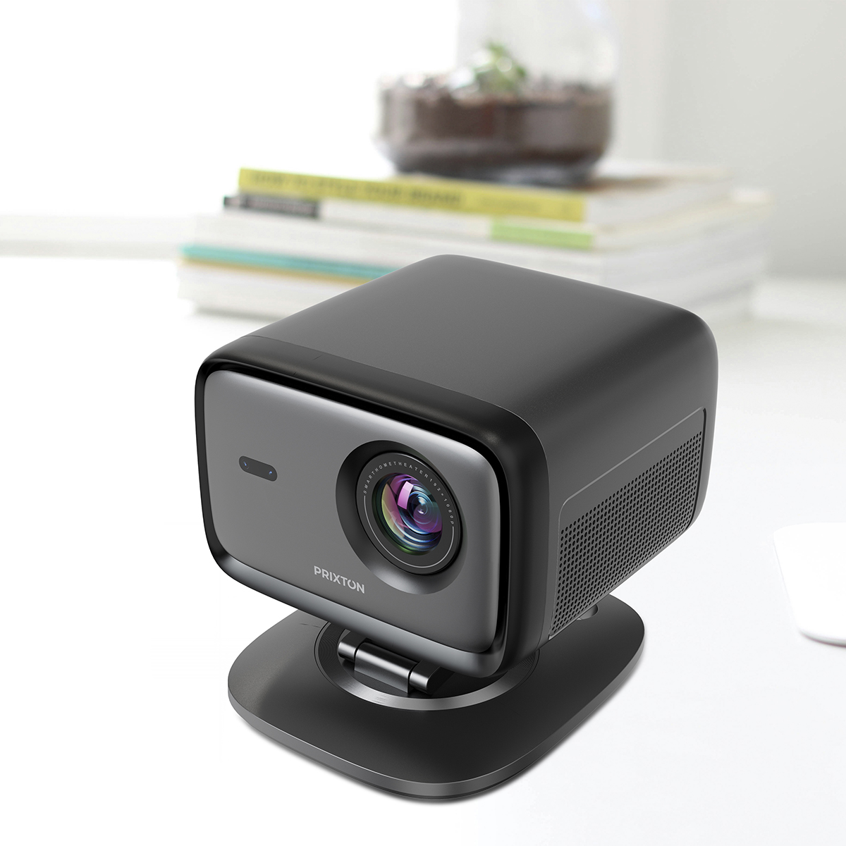 Un proyector compacto y oscuro se asienta sobre un soporte frente a libros y una planta.