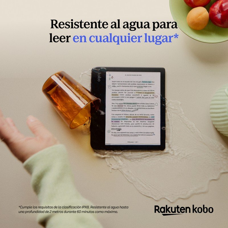Un e-reader Kobo junto a un vaso volcado con líquido ámbar. Frutas al fondo.