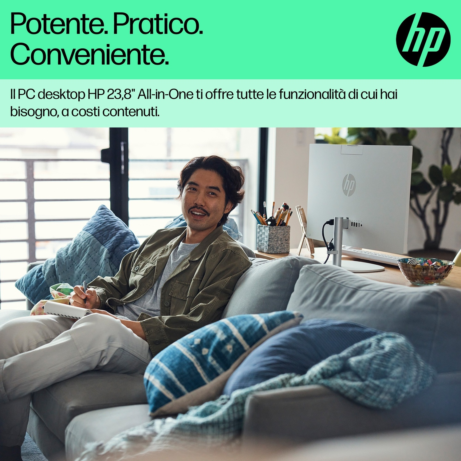 Uomo seduto sul divano scrive su quaderno, PC HP sullo sfondo.
