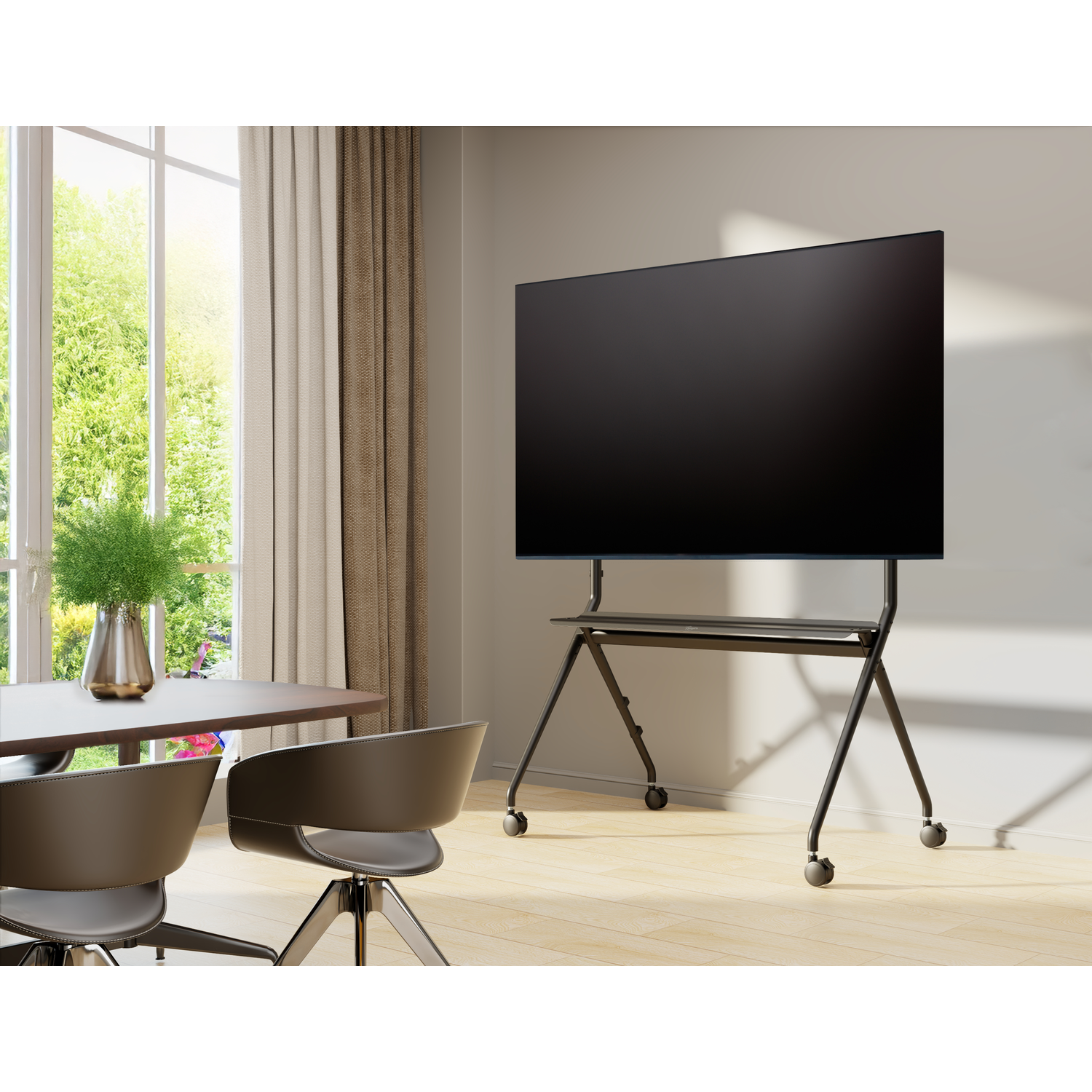 Een grote zwarte tv op een verrijdbaar onderstel in een lichte kamer met eettafel en stoelen.