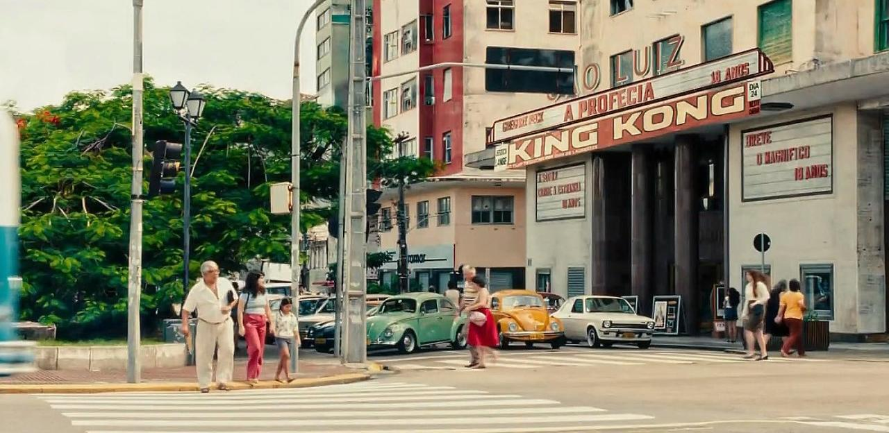 Menschen überqueren eine Straße vor einem Kino, das 'King Kong' zeigt.