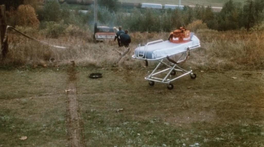 Ein Krankenwagenbett mit roter Tasche steht auf Gras. Zwei Personen stehen daneben.