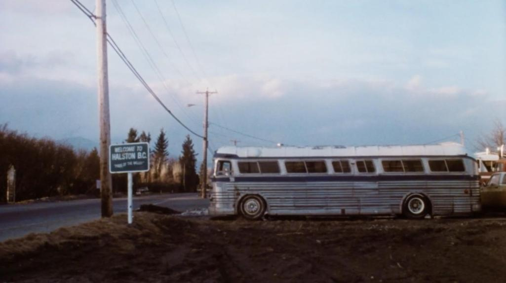 Ein alter, silberblauer Bus steht neben einem Willkommensschild für Halston B.C.