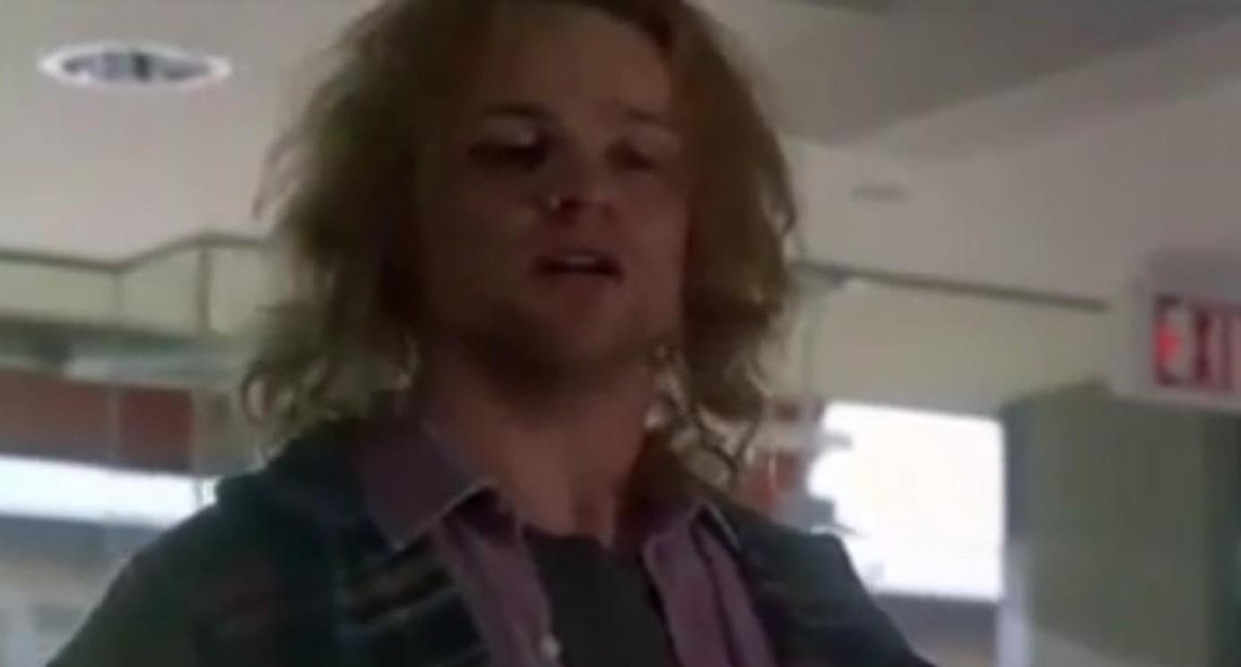 Ein Mann mit langen Haaren trägt ein lila Hemd. Ein rotes 