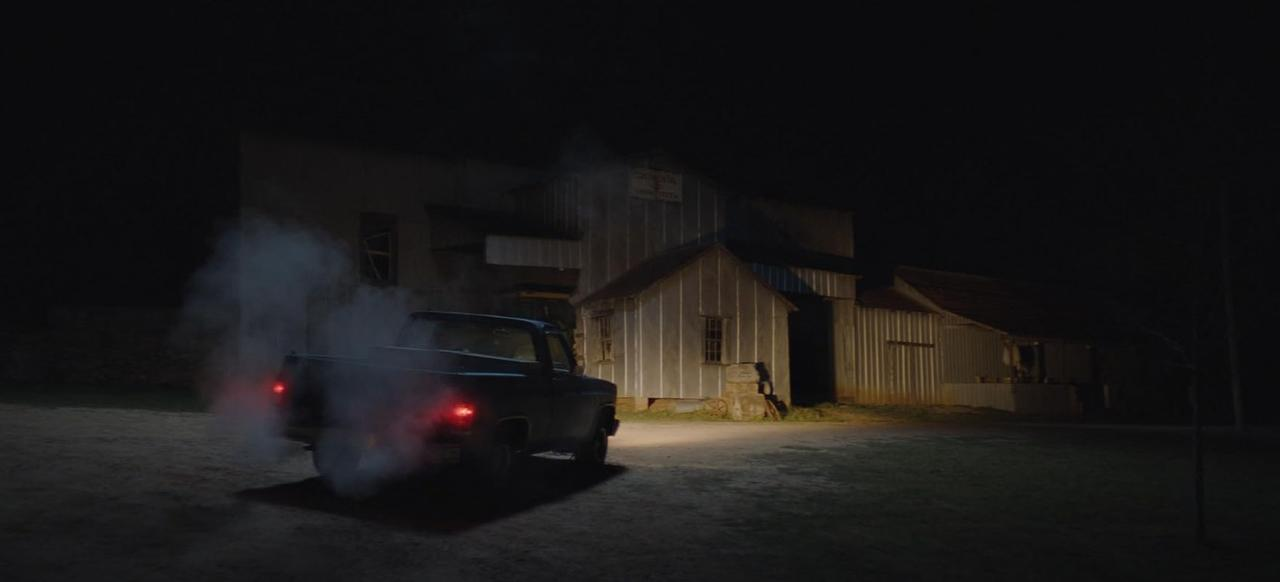 Ein dunkler Pickup mit Rauch und Rücklichtern vor Gebäuden bei Nacht.