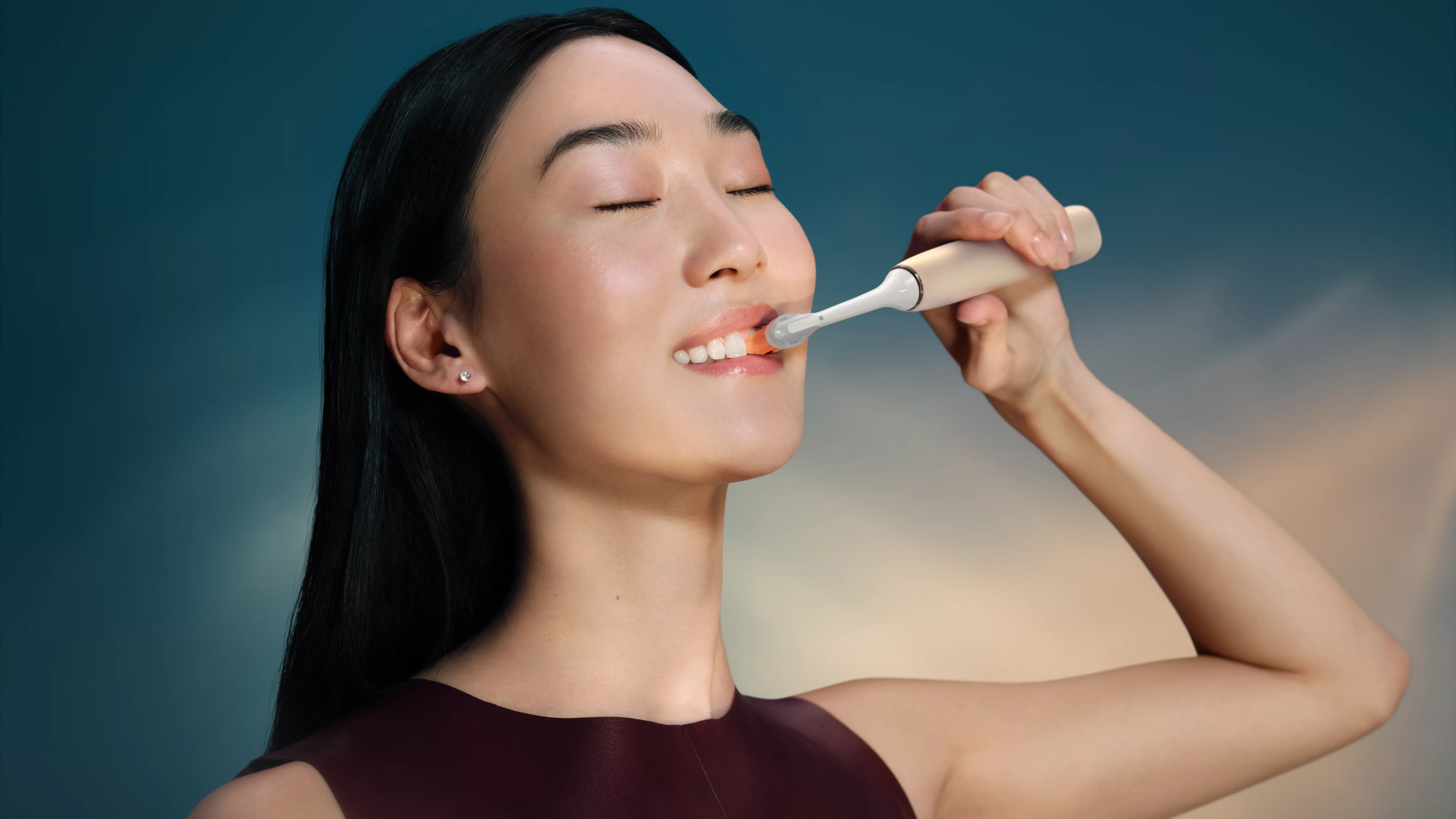 Kobieta myje zęby szczoteczką elektryczną, oczy zamknięte.