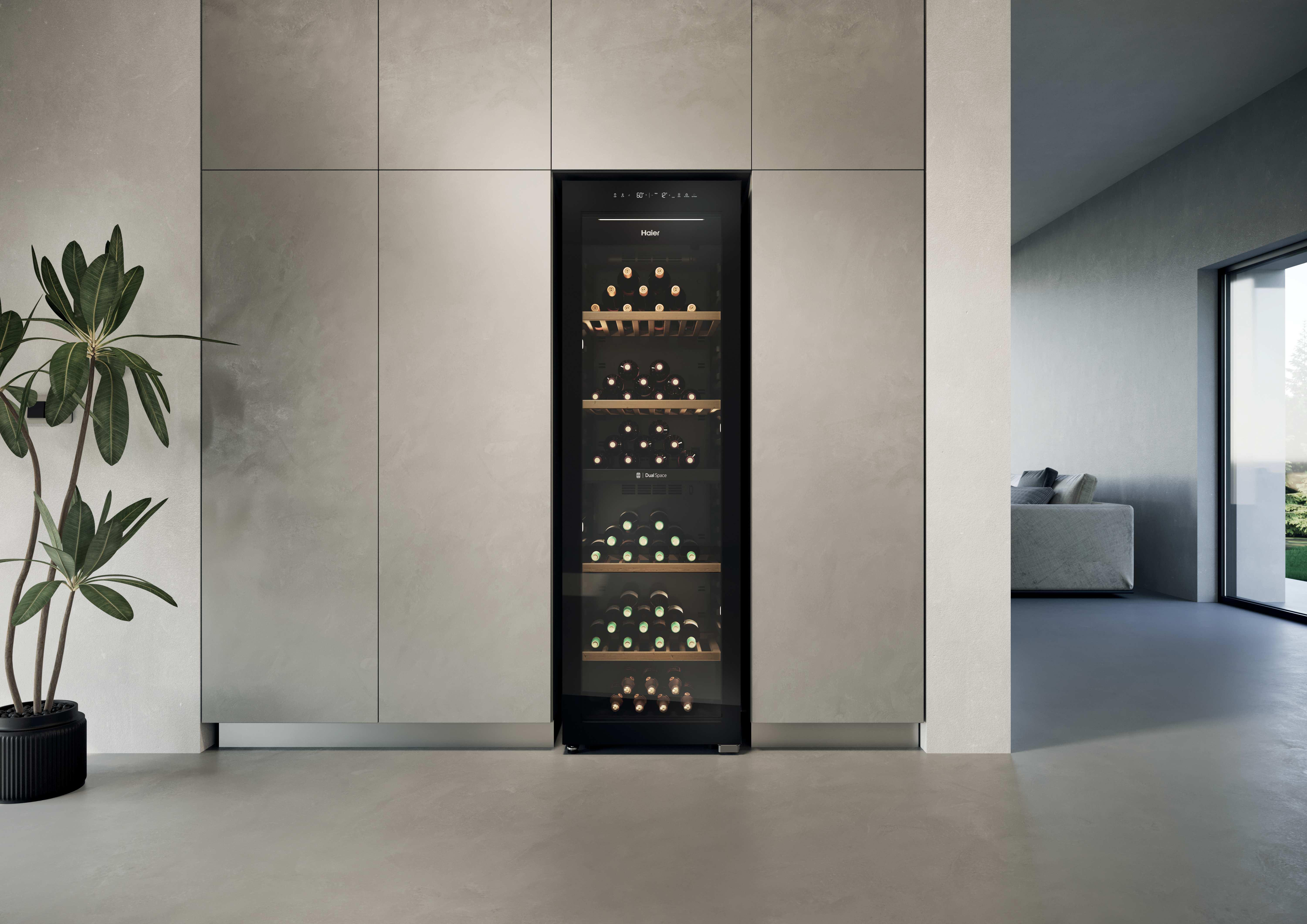 Ein Weinkühlschrank mit Glasfront, gefüllt mit Flaschen, steht neben einer Pflanze.