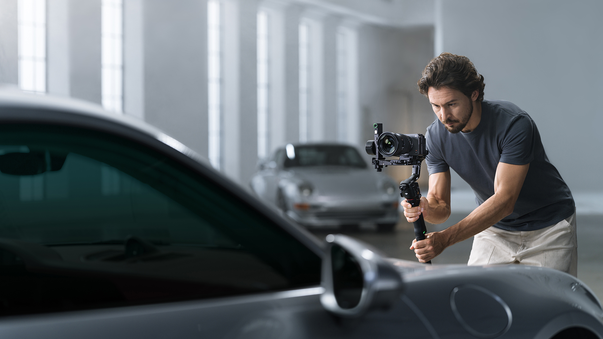 Adam, iki arabanın olduğu aydınlık odada gimbal kamera ile araba çekiyor.