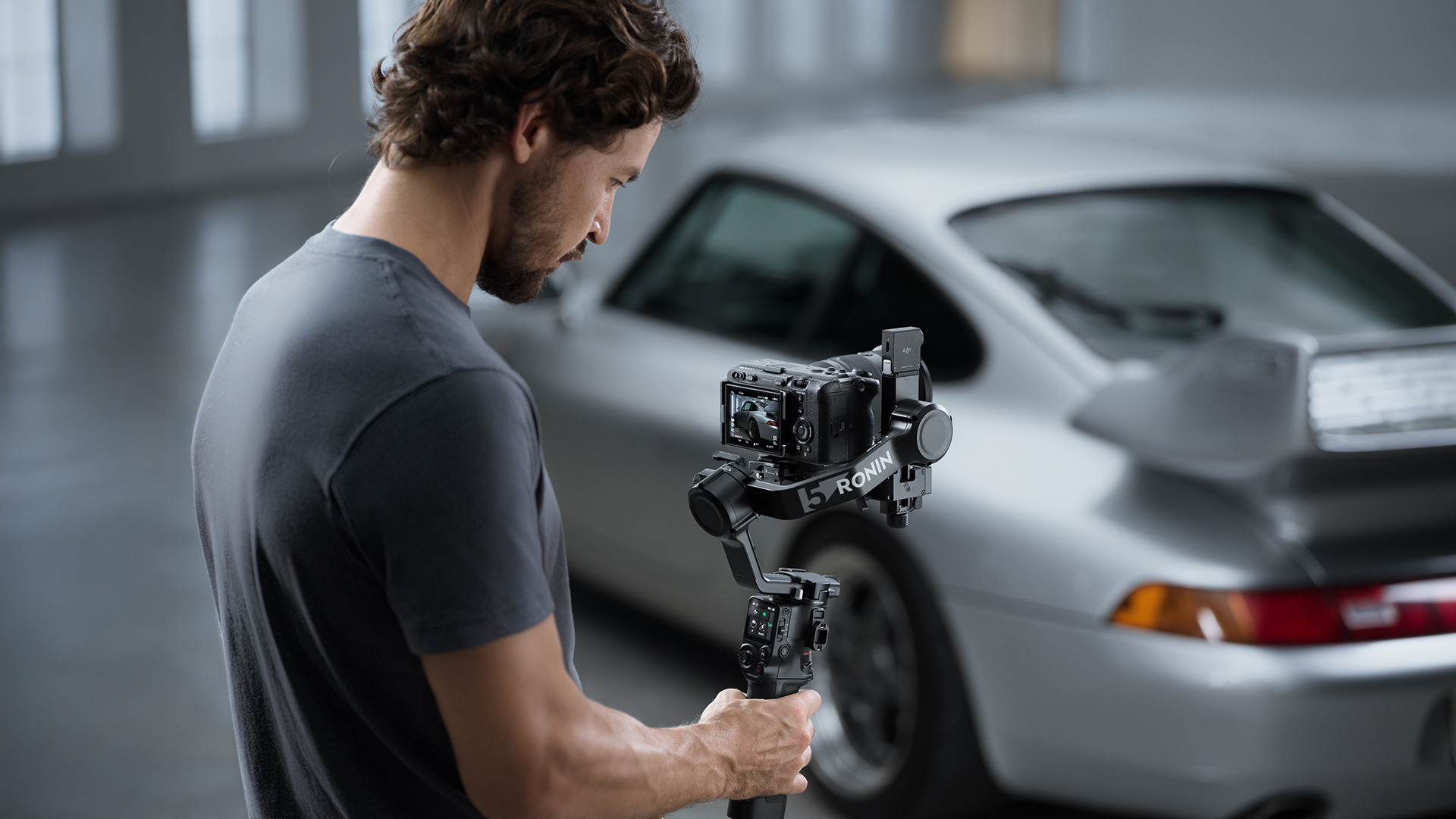 Adam, gimbal sabitleyici üzerindeki bir kamerayla gümüş bir Porsche'yi filme alıyor.