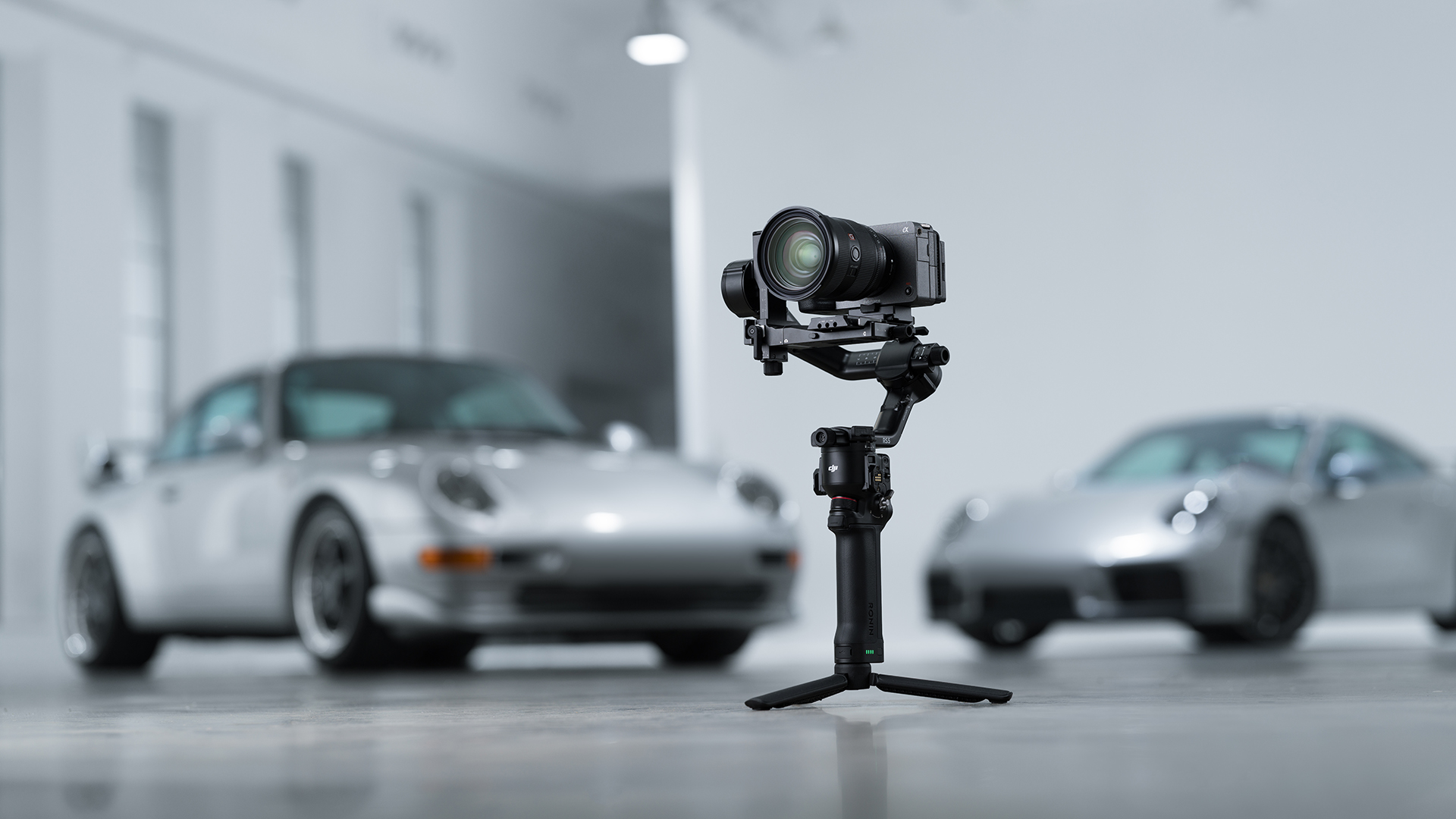 Bir kamera gimbal, bir Showroom'da iki gümüş arabanın önünde duruyor.