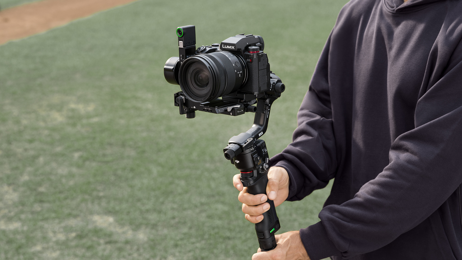 Bir kişi bir sahada dışarıda Lumix kameralı gimbal tutuyor.