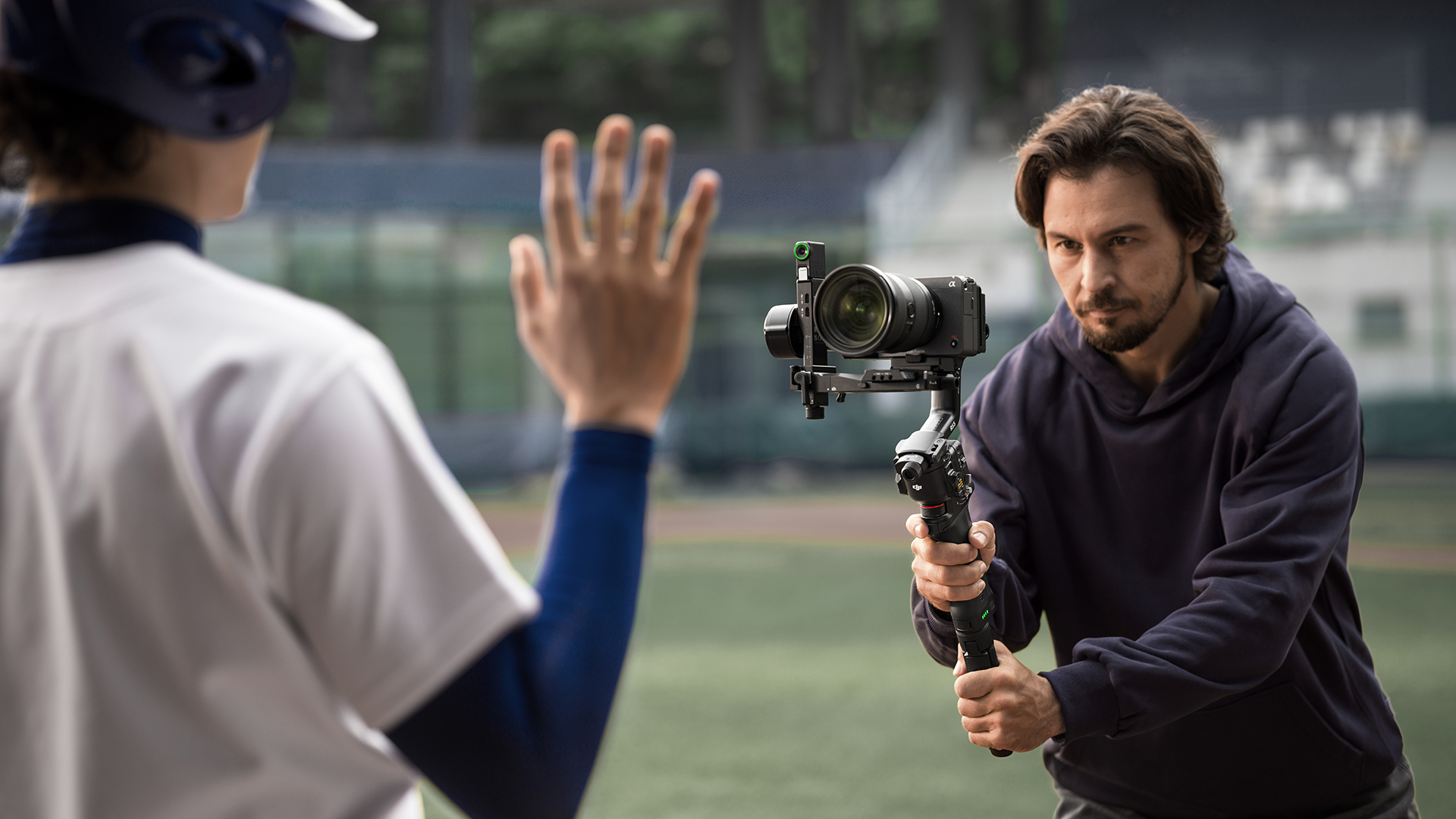 Bir adam gimbal ile bir beyzbol oyuncusunu filme alıyor. Oyuncu elini kaldırıyor.