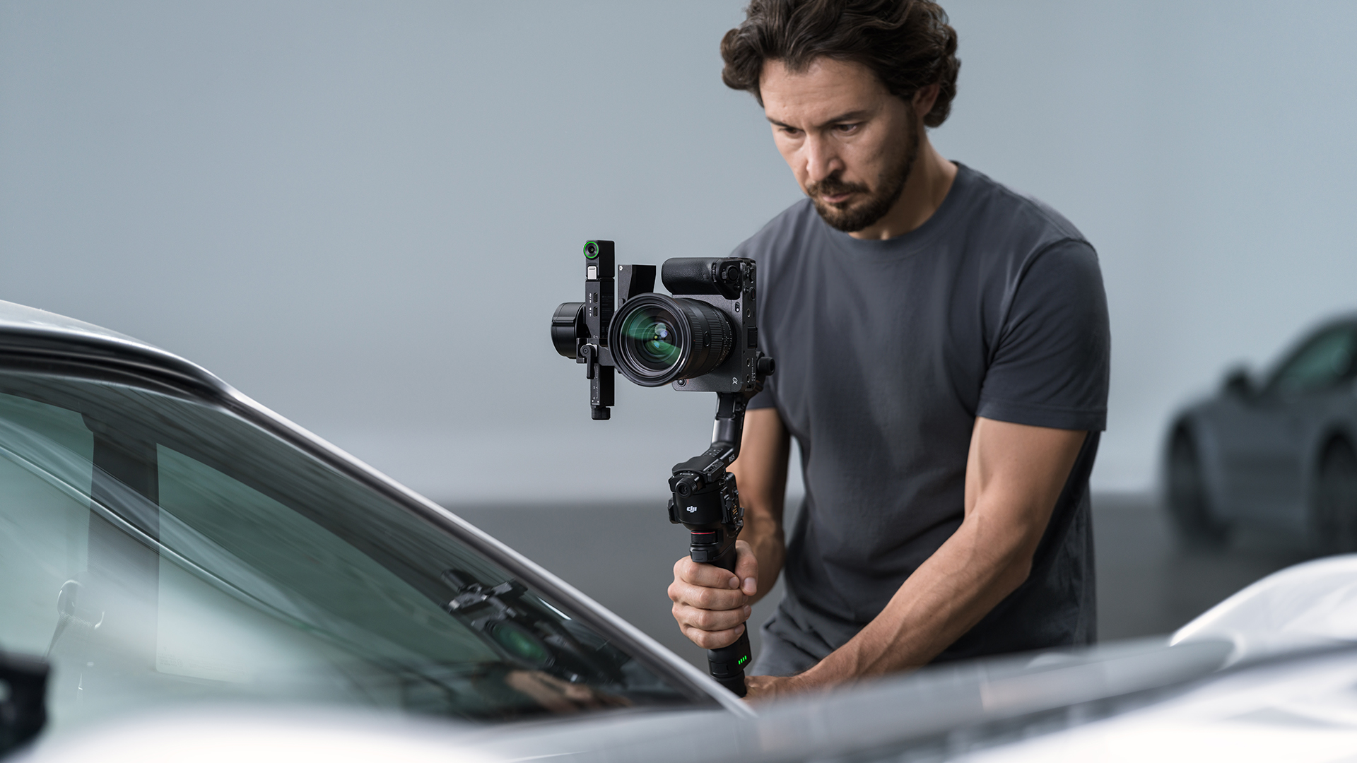 Koyu renk ti00rtl00 bir adam, bir araban00n yan00nda gimbal 00zerinde bir kamera tutuyor.