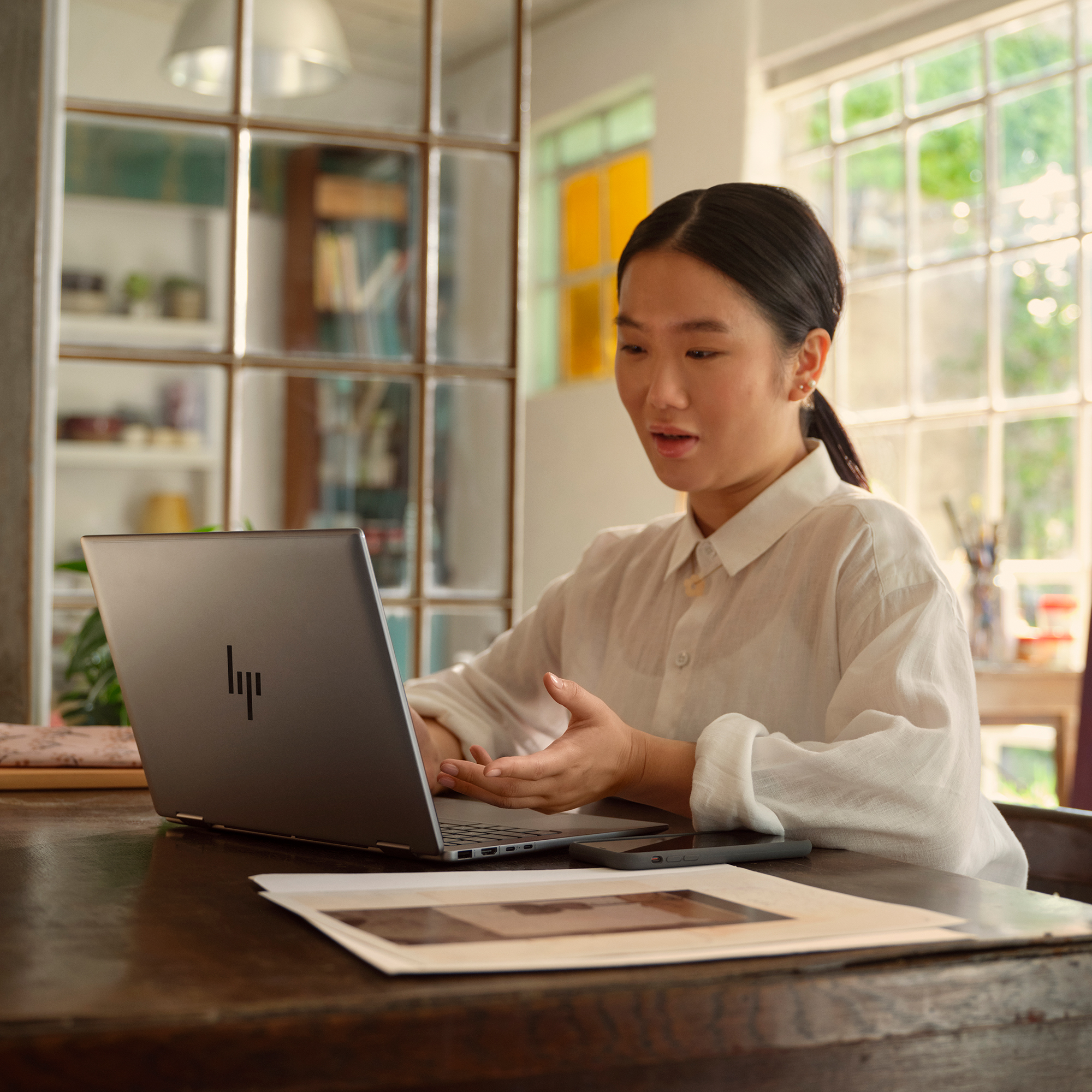 Młoda kobieta w białej koszuli pracuje na laptopie w jasnym pomieszczeniu.