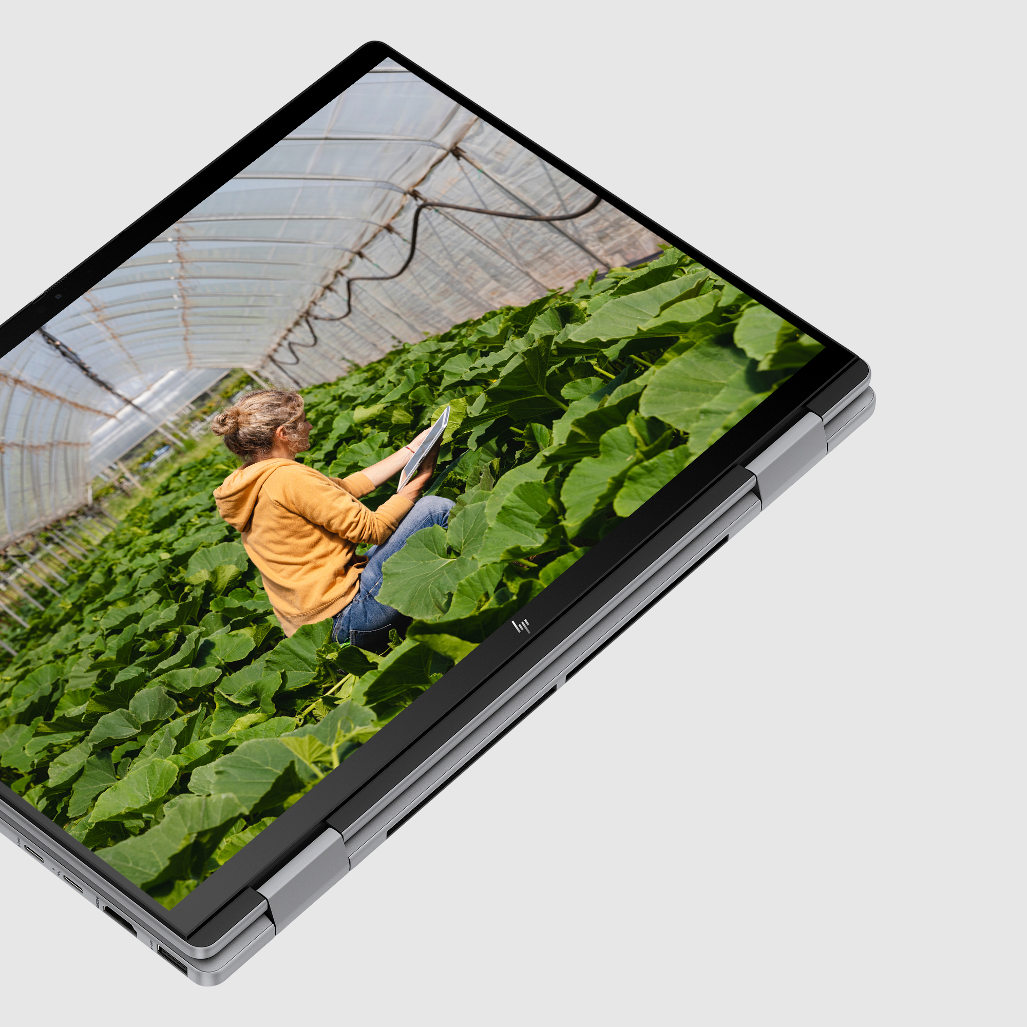 Kobieta w szklarni z bujnymi roślinami, korzystająca z tabletu.