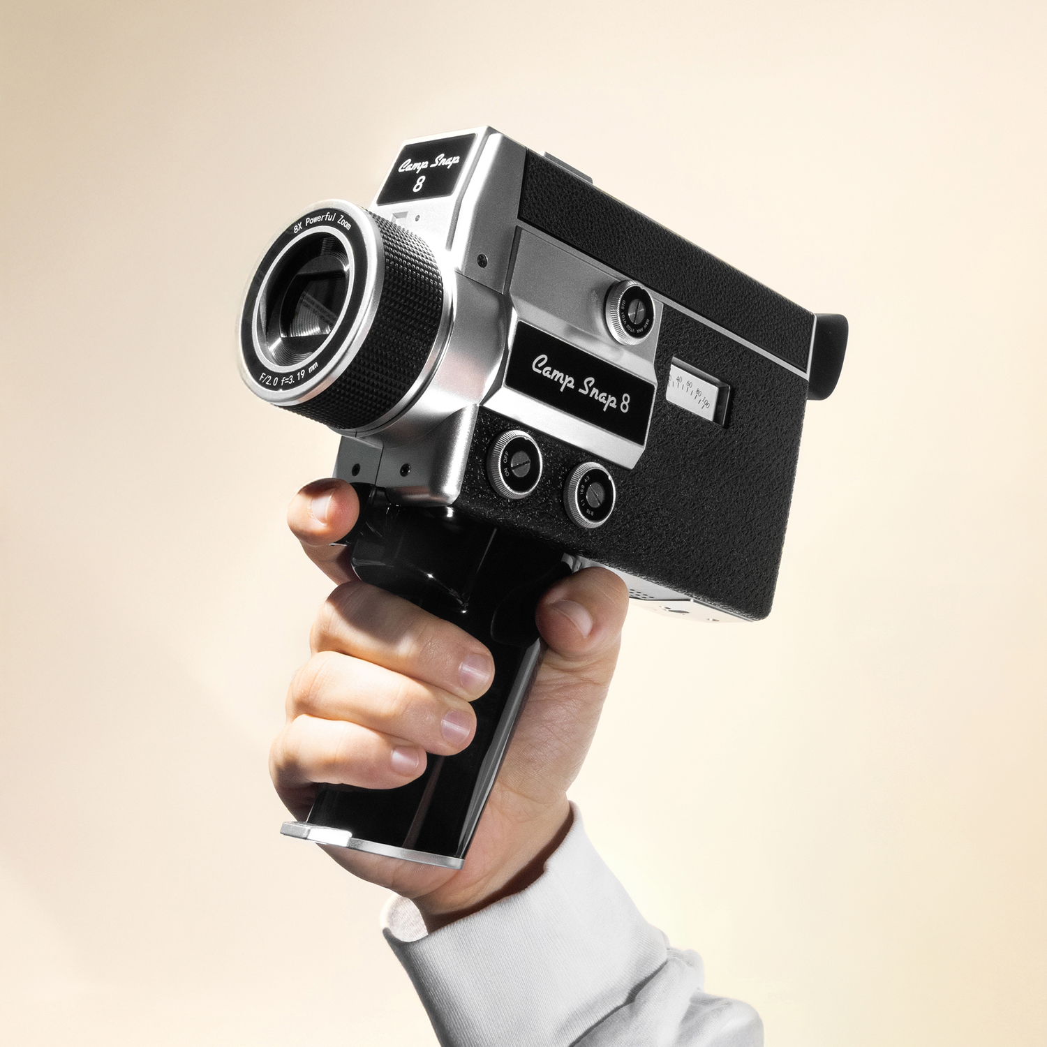Een hand houdt een zilveren en zwarte Super 8 camera vast met het label "Camp Snap 8".