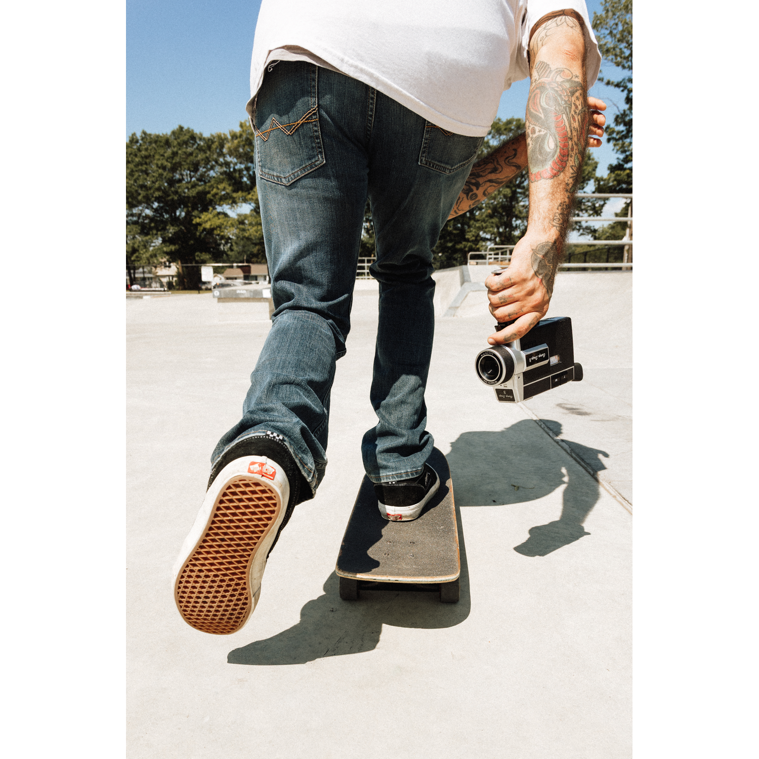 Persoon op skateboard houdt camera vast. Bomen en lucht op achtergrond.