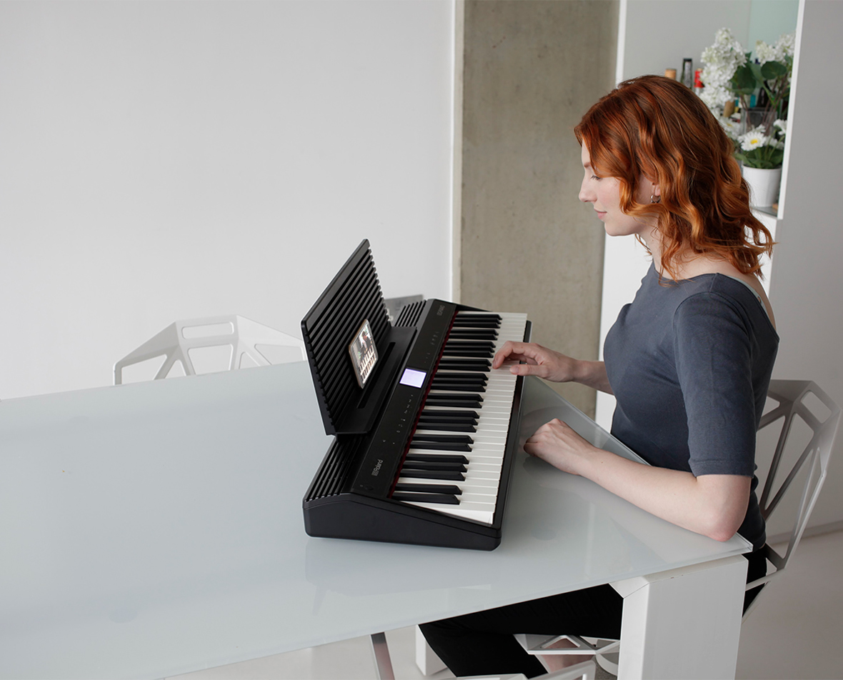 Une femme aux cheveux roux joue d'un clavier noir à une table en verre.