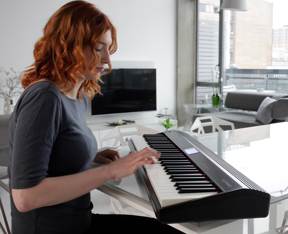 Une femme aux cheveux roux joue d'un piano numérique dans un salon moderne.