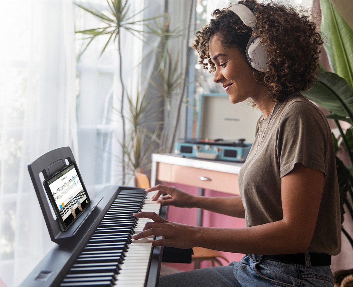 Femme avec casque joue du clavier, partitions sur tablette.