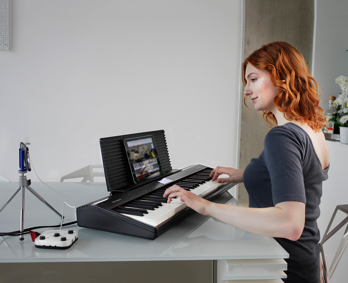 Une femme aux cheveux roux joue d'un clavier avec une tablette montée dessus.