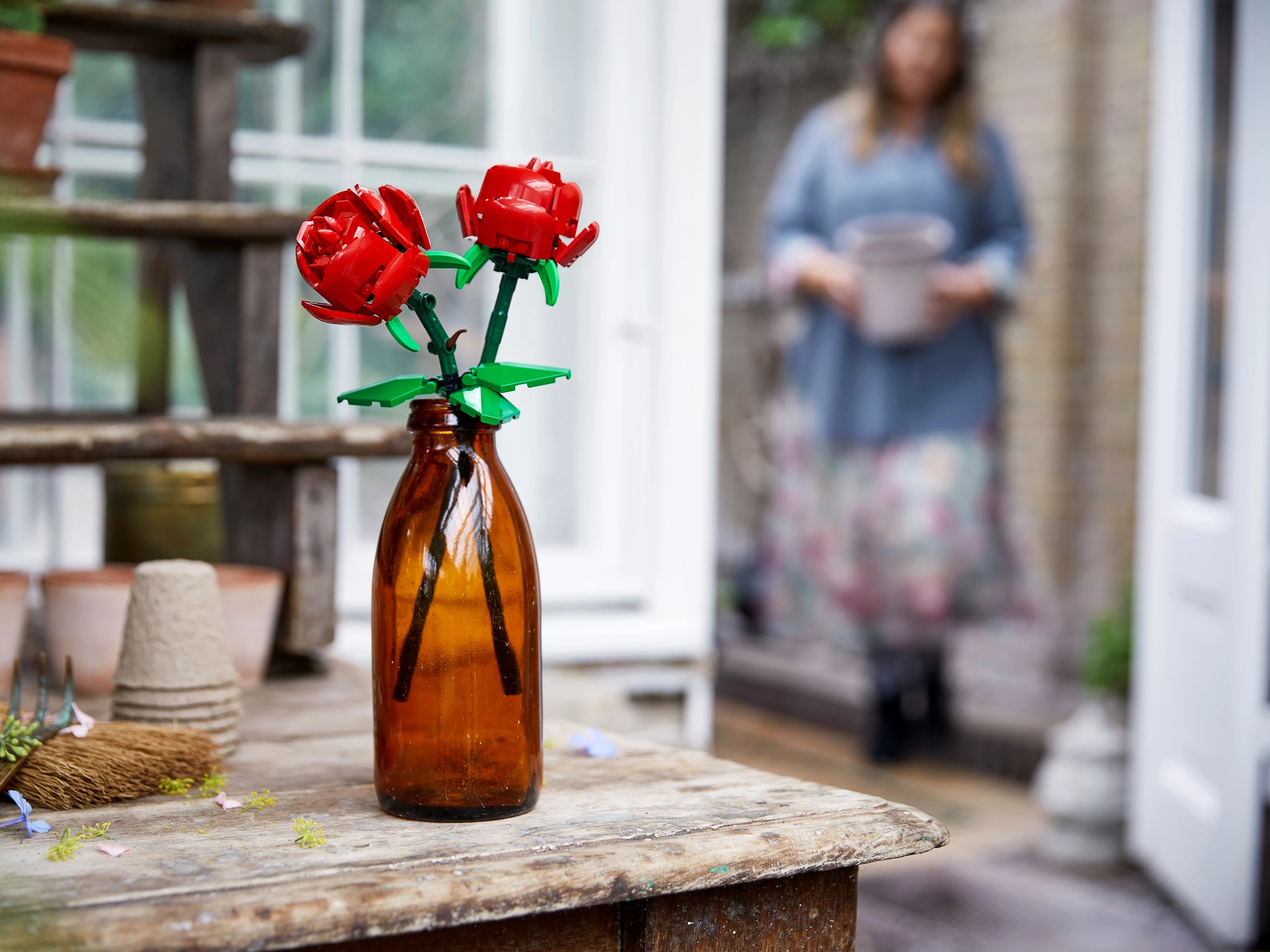 Dwie czerwone róże Lego w brązowej szklanej butelce na drewnianym stole.