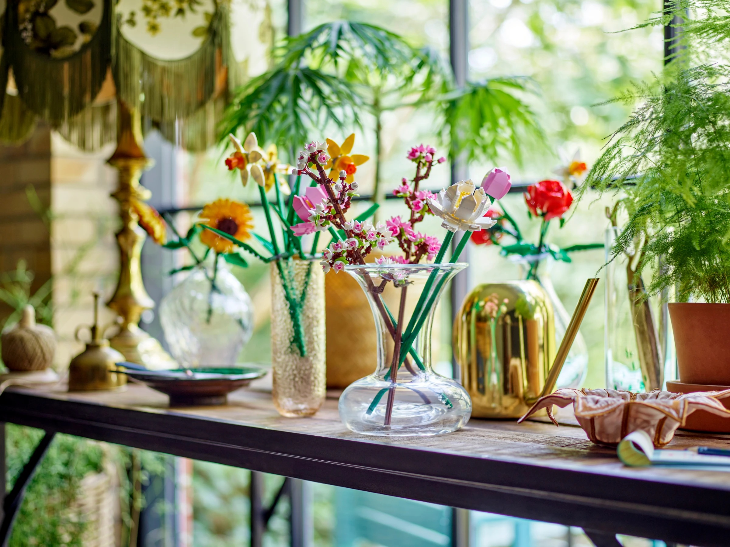 Kolorowe kwiaty Lego w szklanych wazonach na półce przy oknie.