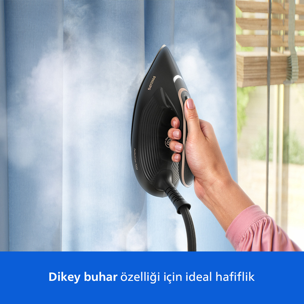 Bir el, buhar çıkaran siyah buharlı ütüyü mavi bir perdeye doğrultuyor.