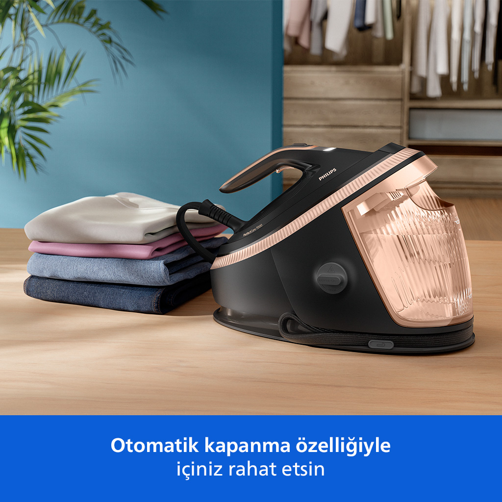 Ahşap bir masada, üst üste konulmuş kıyafetlerin yanında, rose gold detaylı siyah buharlı ütü.