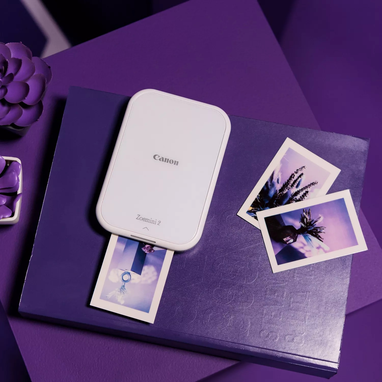 Biała drukarka Canon ze zdjęciami na fioletowej książce.