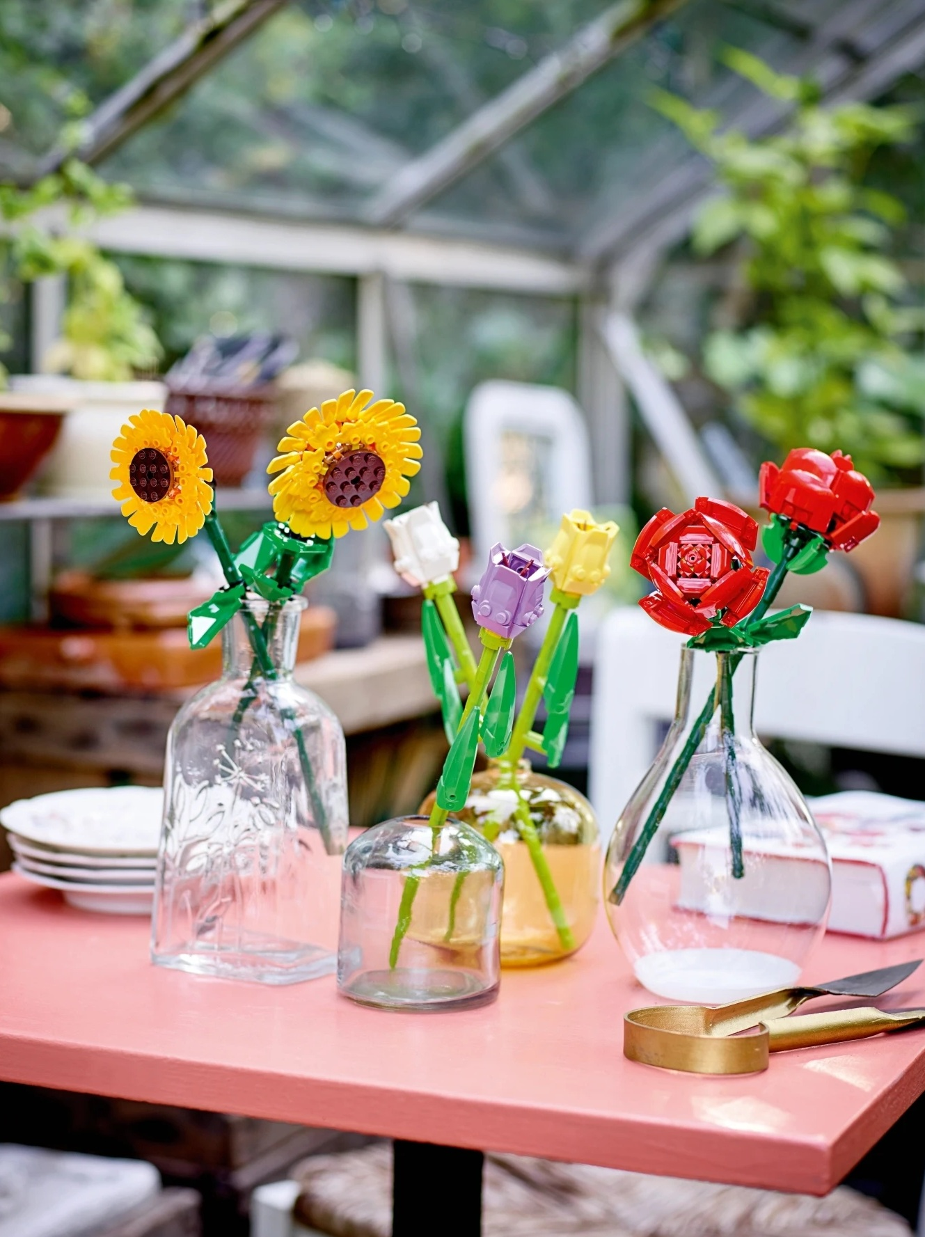 Kolorowe kwiaty Lego w szklanych wazonach na stole w szklarni.