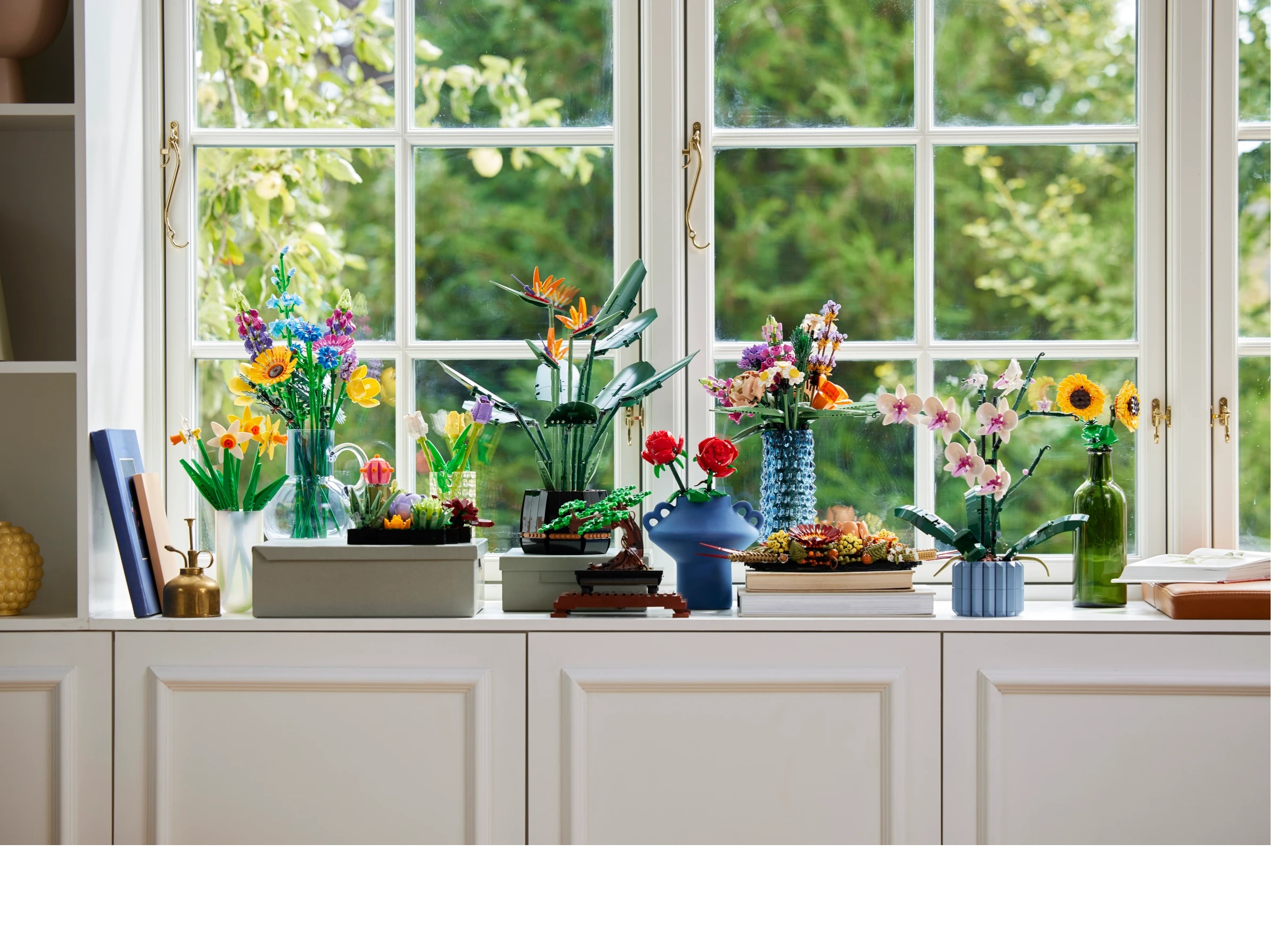 Aranżacje kwiatowe na parapecie z widocznymi przez okno drzewami.